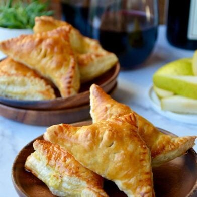Mini Fruit and Cheese Turnovers on brown plate with glasses of red wine in background