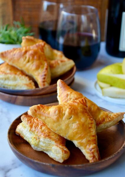 Mini Fruit and Cheese Turnovers on brown plate with glasses of red wine in background