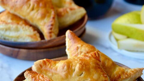 Mini Fruit and Cheese Turnovers on brown plate with glasses of red wine in background