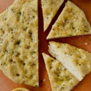 Four slices of Easy Homemade Focaccia (No Yeast) next to small bowls containing kosher salt and olive oil.