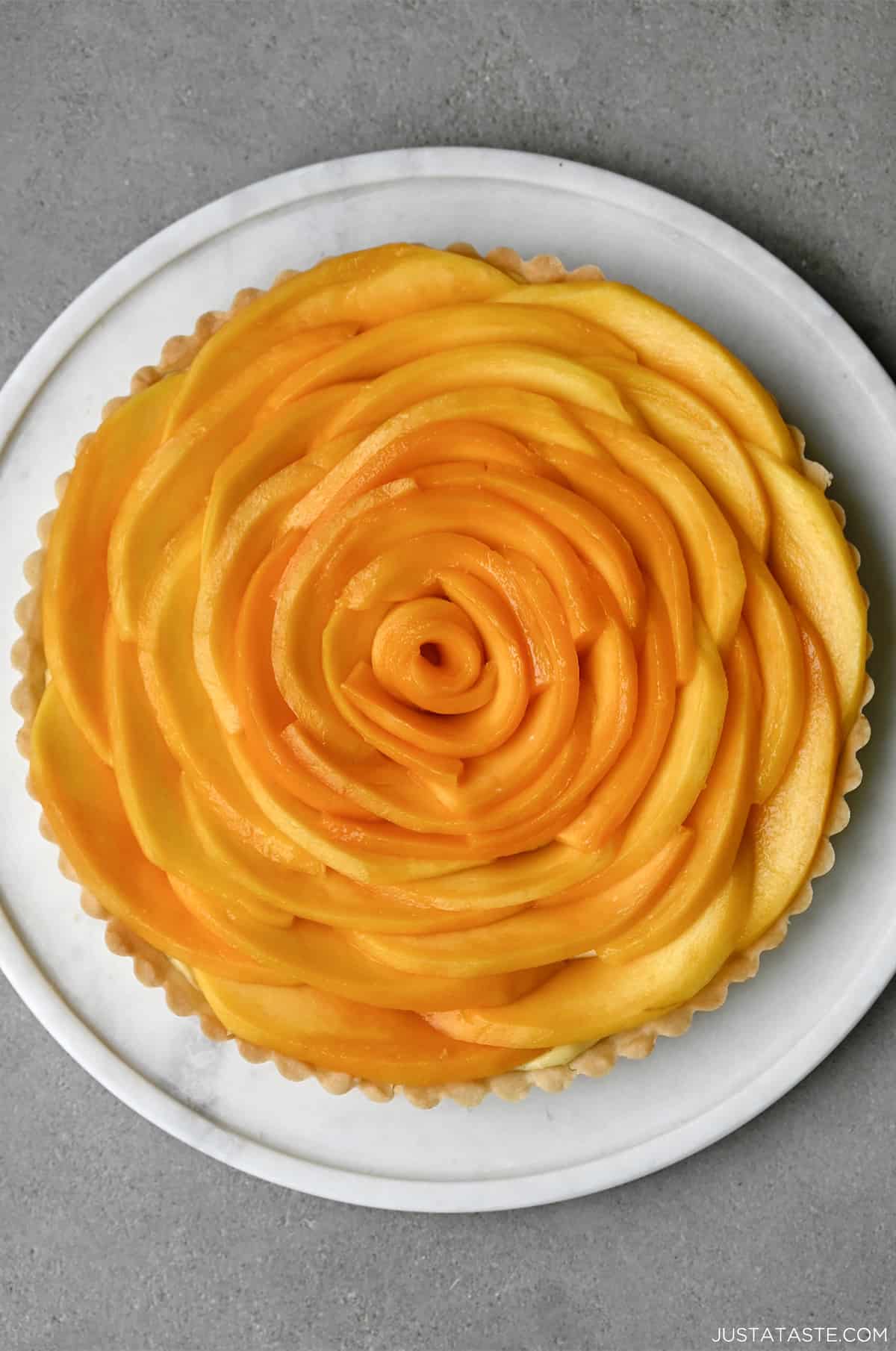 Easy mango tart with vanilla bean pastry cream on a white pie plate.