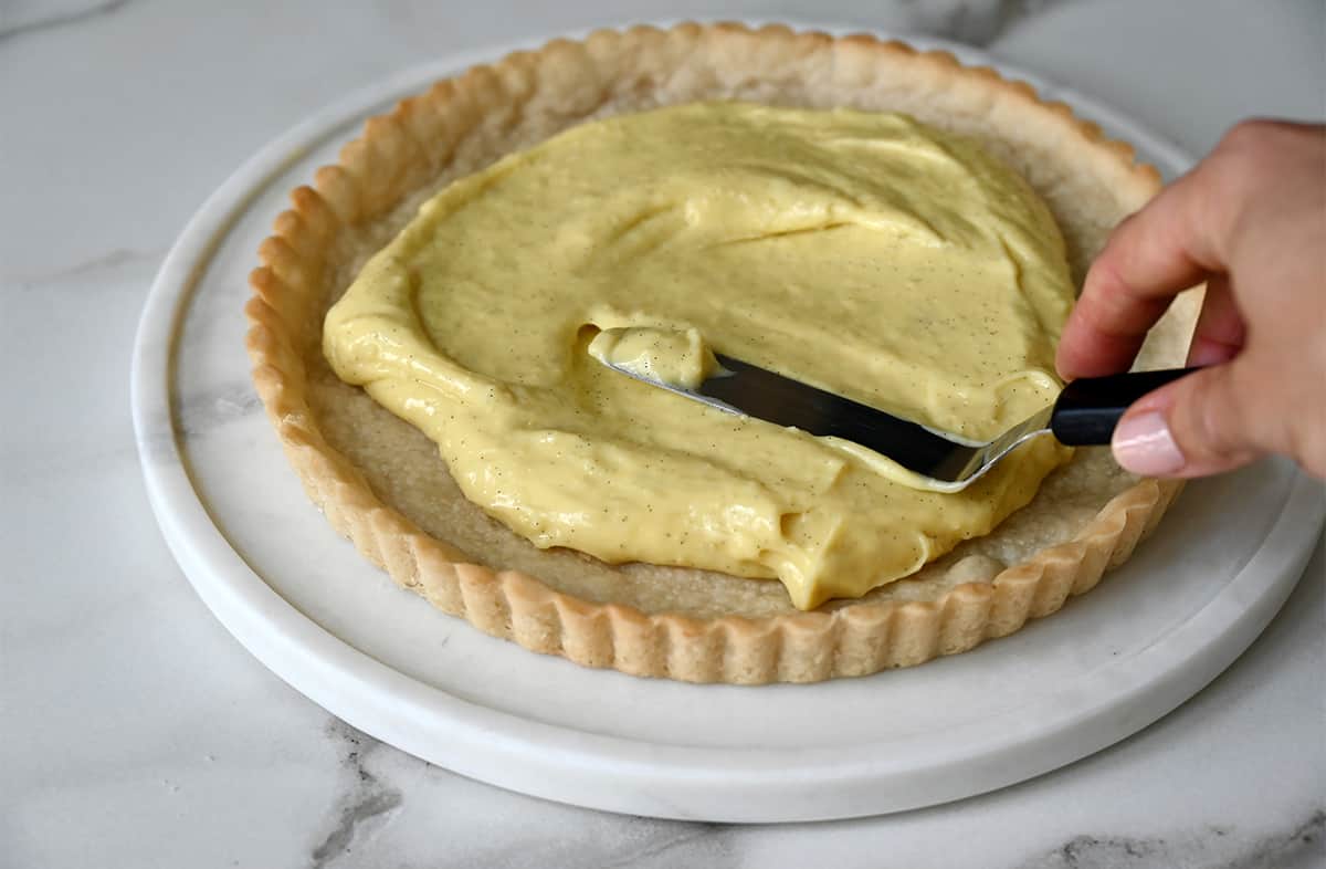 Vanilla pastry cream being spread atop a shortbread crust with an offset spatula.