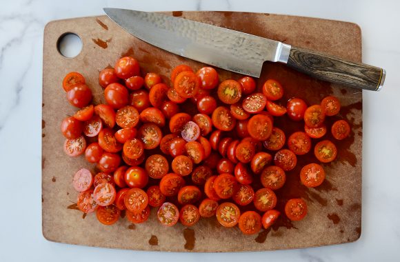 Sliced cherry tomatoes on cutting board next to sharp knife
