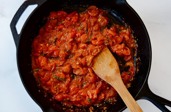 Wooden spoon in large skillet with cooked down tomatoes