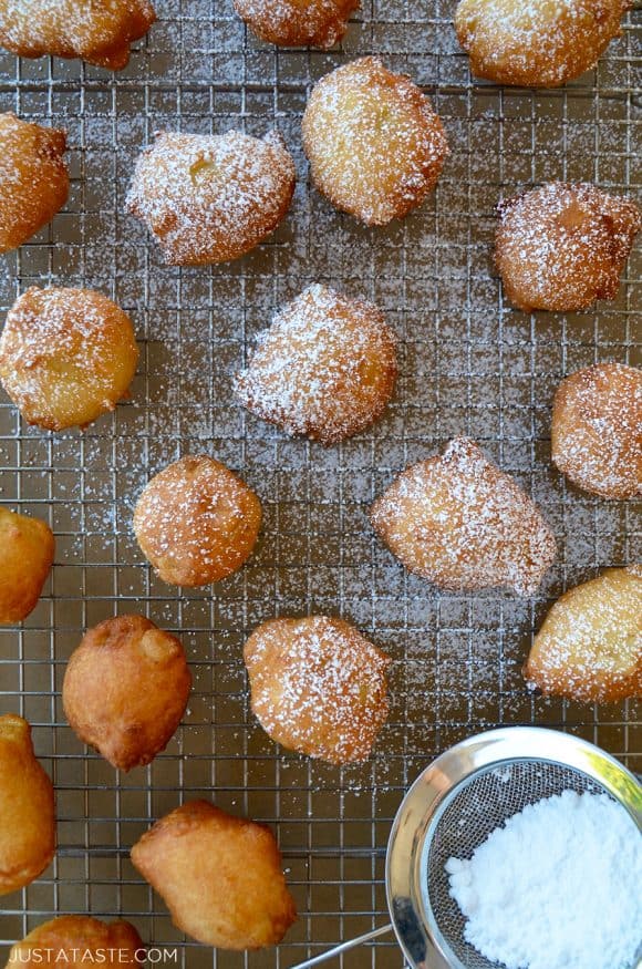 Top down view of easy apple fritters on baking sheet next to hand sifter containing confectioners' sugar