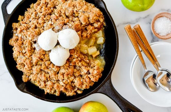 Homemade apple and pear crisp topped with ice cream next to plate with spoons