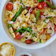 A top-down view of a large white bowl containing Asparagus Pasta Salad with cherry tomatoes, red pepper flakes and red onion.