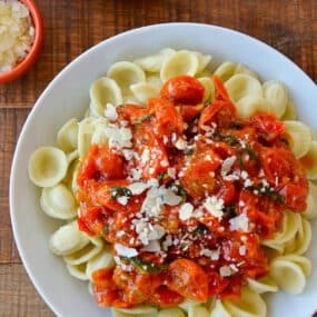 Cherry tomato pasta sauce over noodles on a white plate.
