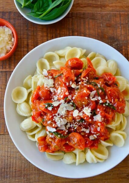 Cherry tomato pasta sauce over noodles on a white plate.
