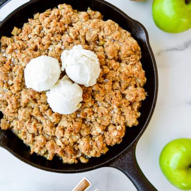 Homemade apple and pear crisp topped with vanilla ice cream next to green apples