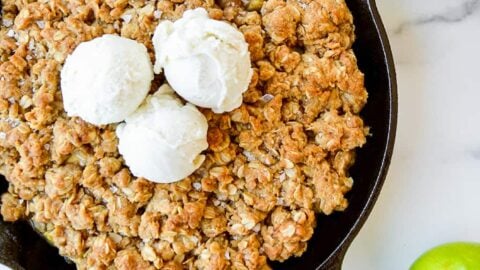 Homemade apple and pear crisp topped with vanilla ice cream next to green apples