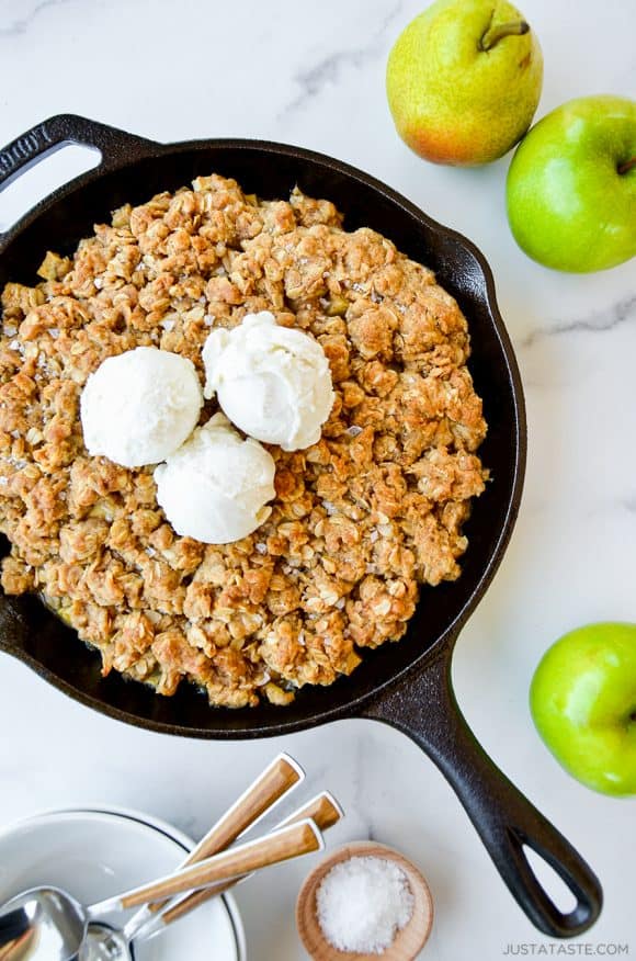 Homemade apple and pear crisp topped with vanilla ice cream next to green apples