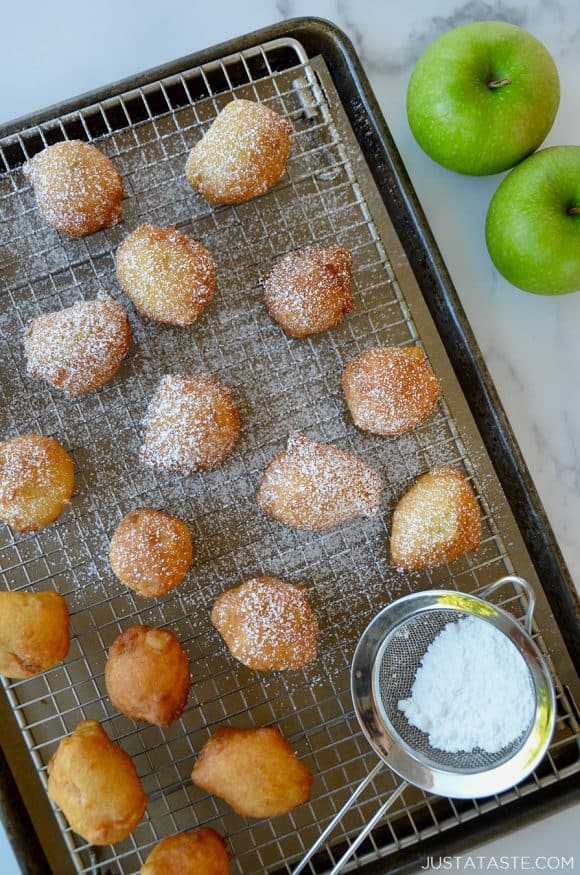 30-Minute Apple Fritters dusted with confectioners' sugar on baking sheet next to Granny smith apples