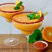 An orange and mango margarita in glasses with rims lined with tajin seasoning