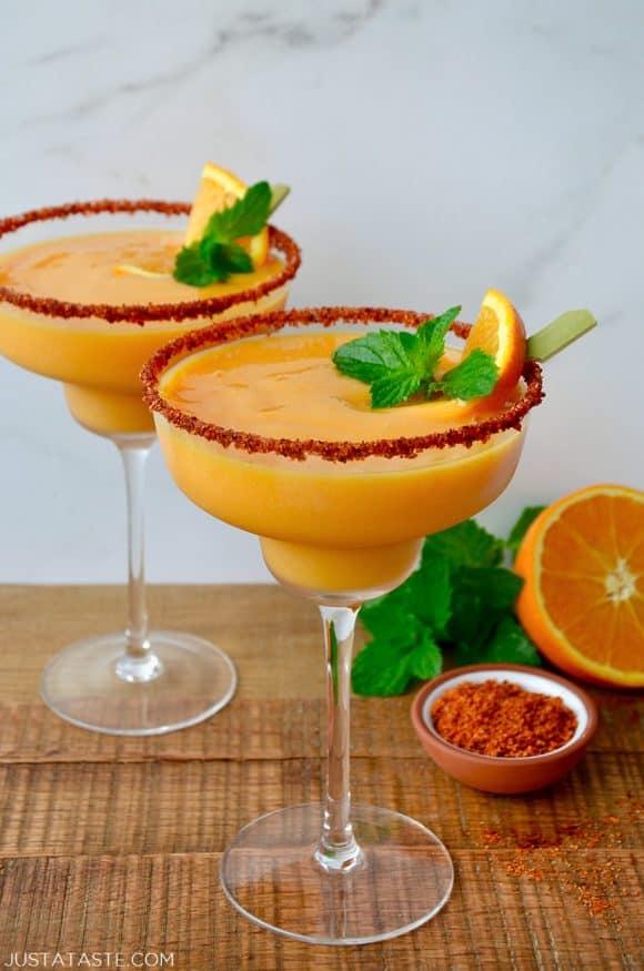 An orange and mango margarita in glasses with rims lined with tajin seasoning