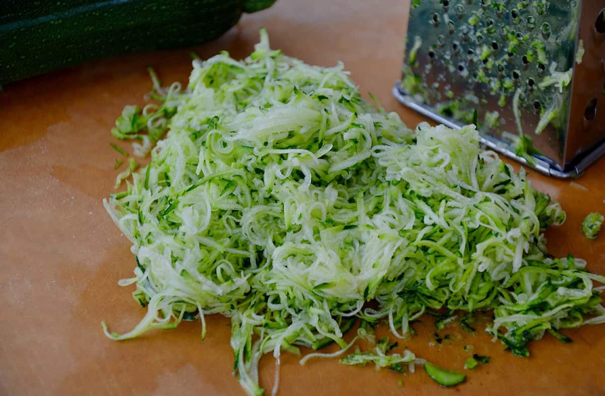 Finely shredded zucchini next to a box grater.