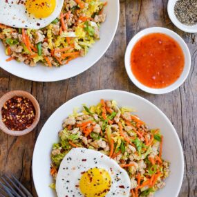 Two servings of Healthy Egg Roll In a Bowl topped with a fried egg next to small ramekins with spices