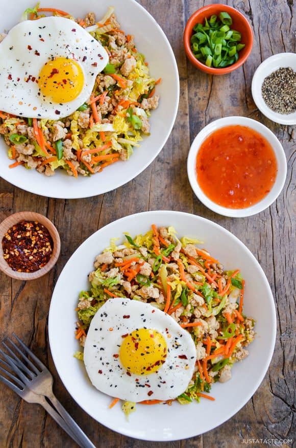 Two servings of Healthy Egg Roll In a Bowl topped with a fried egg next to small ramekins with spices