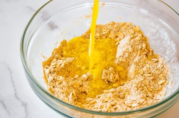 Melted butter being poured over dry ingredients in clear bowl