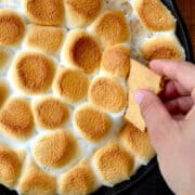 A hand dipping a graham cracker into a skillet containing Peanut Butter Cup S'mores Dip.