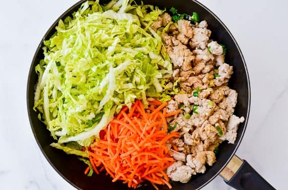 Skillet containing ground chicken, sliced carrots and shredded cabbage