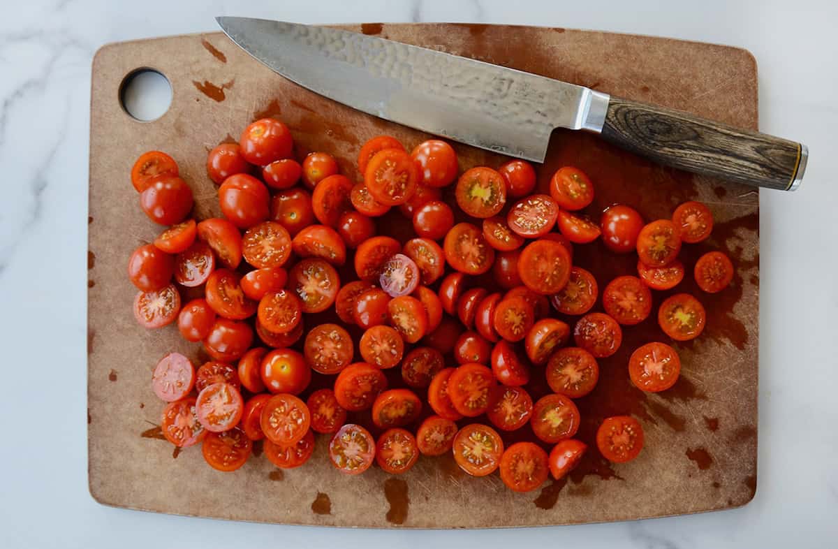 Halved cherry tomatoes on a cutting board with a chef's knife.