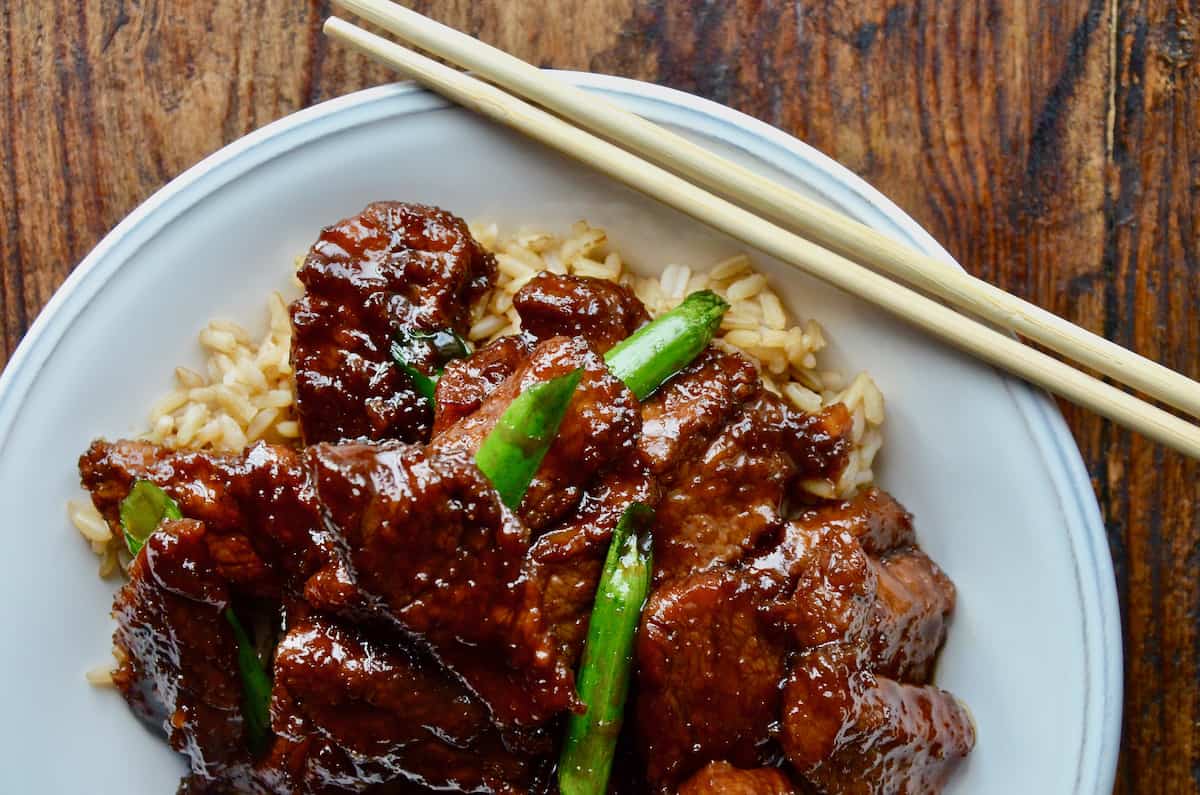 Mongolian beef over brown rice on a dinner plate with chopsticks.
