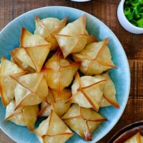 Top down view of Crispy Baked Crab Rangoon on blue plate next to small ramekin containing sweet and sour sauce