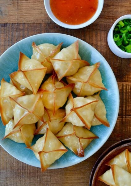 Top down view of Crispy Baked Crab Rangoon on blue plate next to small ramekin containing sweet and sour sauce