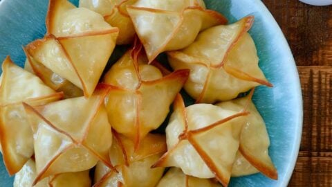 Top down view of Crispy Baked Crab Rangoon on blue plate next to small ramekin containing sweet and sour sauce