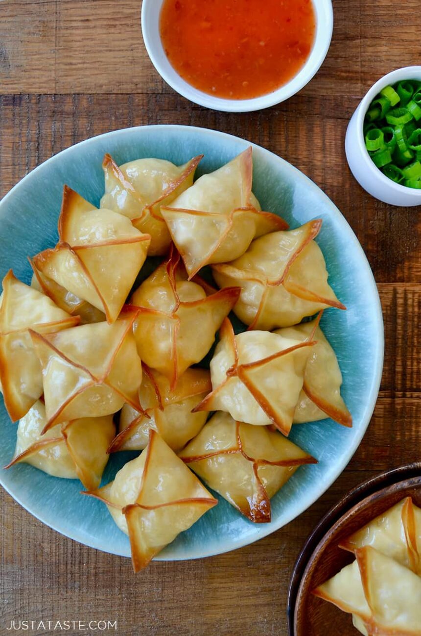 Top down view of Crispy Baked Crab Rangoon on blue plate next to small ramekin containing sweet and sour sauce