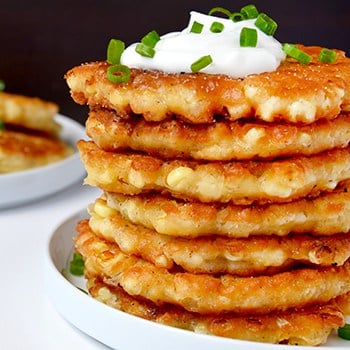 A stack of corn fritters topped with sour cream and chives