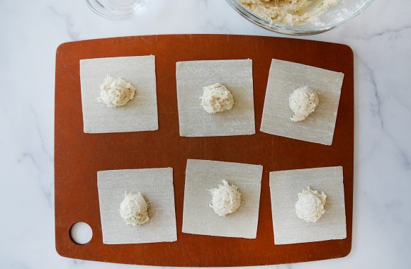 Wonton wrappers containing crab mixture atop wood cutting board