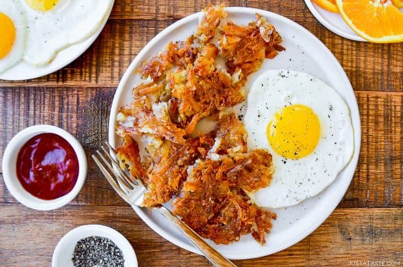 Easy crispy hash browns on white plate with a fried egg next to small ramekins containing pepper and ketchup