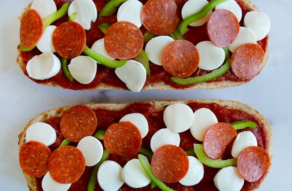 Unbaked French bread pizza topped with green peppers, pepperoni and mozzarella