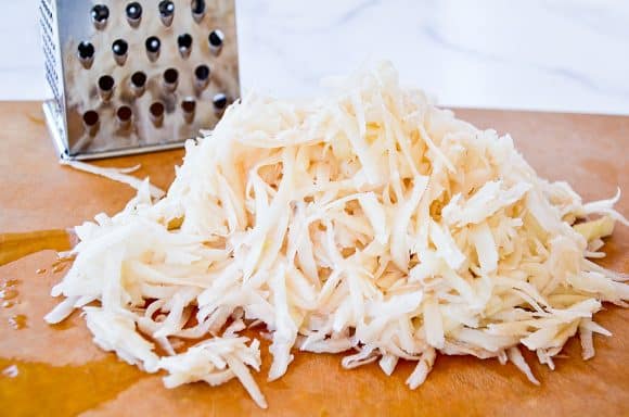 Shredded potatoes on a cutting board next to a box grater