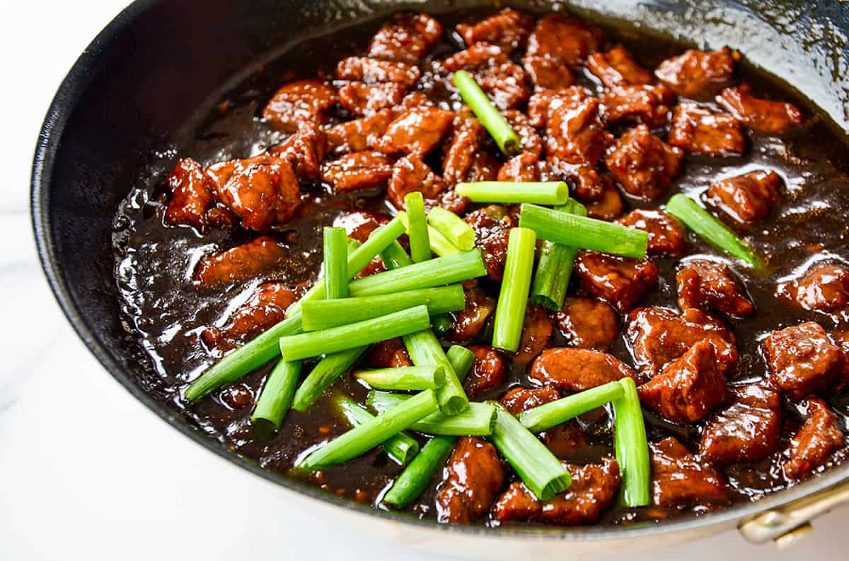 Cooked flank steak in a sweet and savory stir fry sauce topped with sliced fresh scallions.