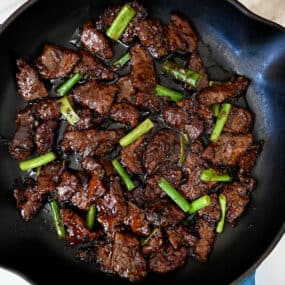 A large skillet containing Mongolian beef with sliced scallions.