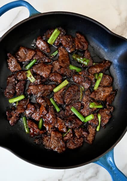A large skillet containing Mongolian beef with sliced scallions.