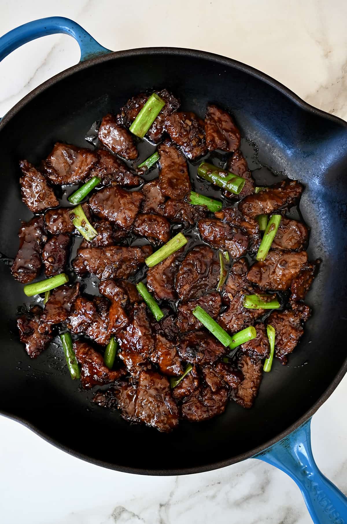 A large skillet containing Mongolian beef with sliced scallions.