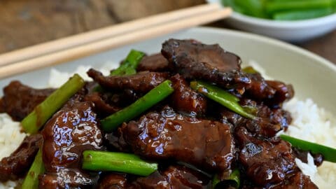 Mongolian beef with sliced scallions atop steamed white rice in a white bowl with chopsticks.