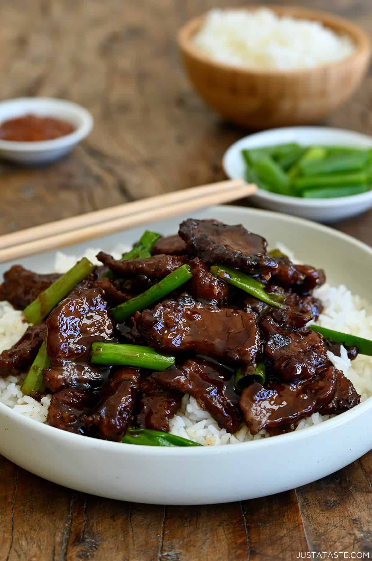 Mongolian beef with sliced scallions atop steamed white rice in a white bowl with chopsticks.