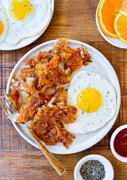 Top down view of a white plate containing the best crispy hash browns, a fork and a fried egg