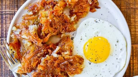 Top down view of a white plate containing the best crispy hash browns, a fork and a fried egg