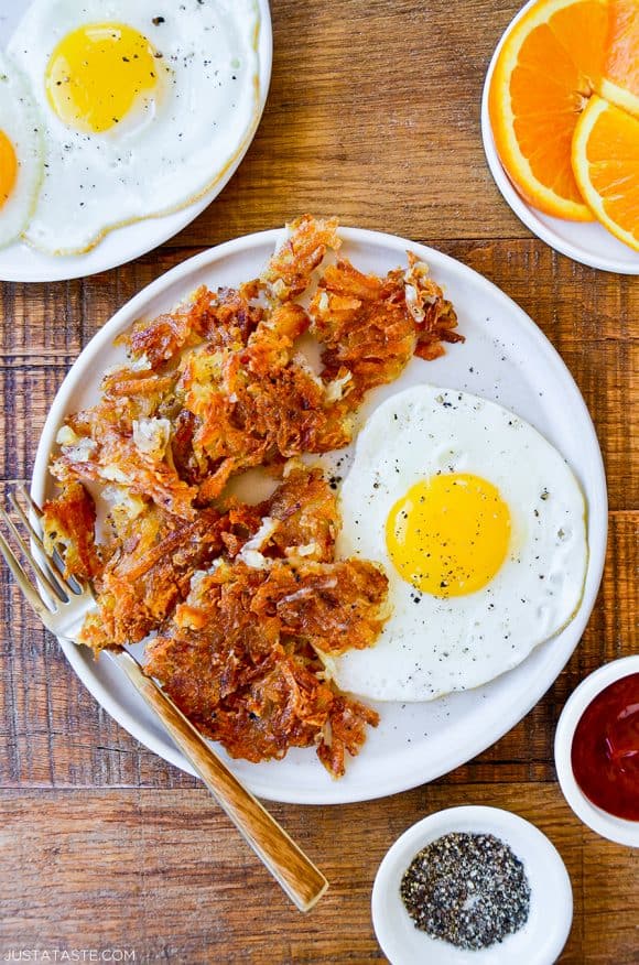 Top down view of a white plate containing the best crispy hash browns, a fork and a fried egg