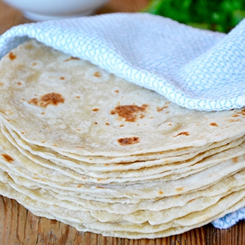 A stack of homemade flour tortillas wrapped in a blue towel