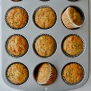 A top-down view of a muffin tin containing freshly baked zucchini banana muffins.