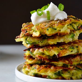 A stack of zucchini fritters topped with sour cream and scallions