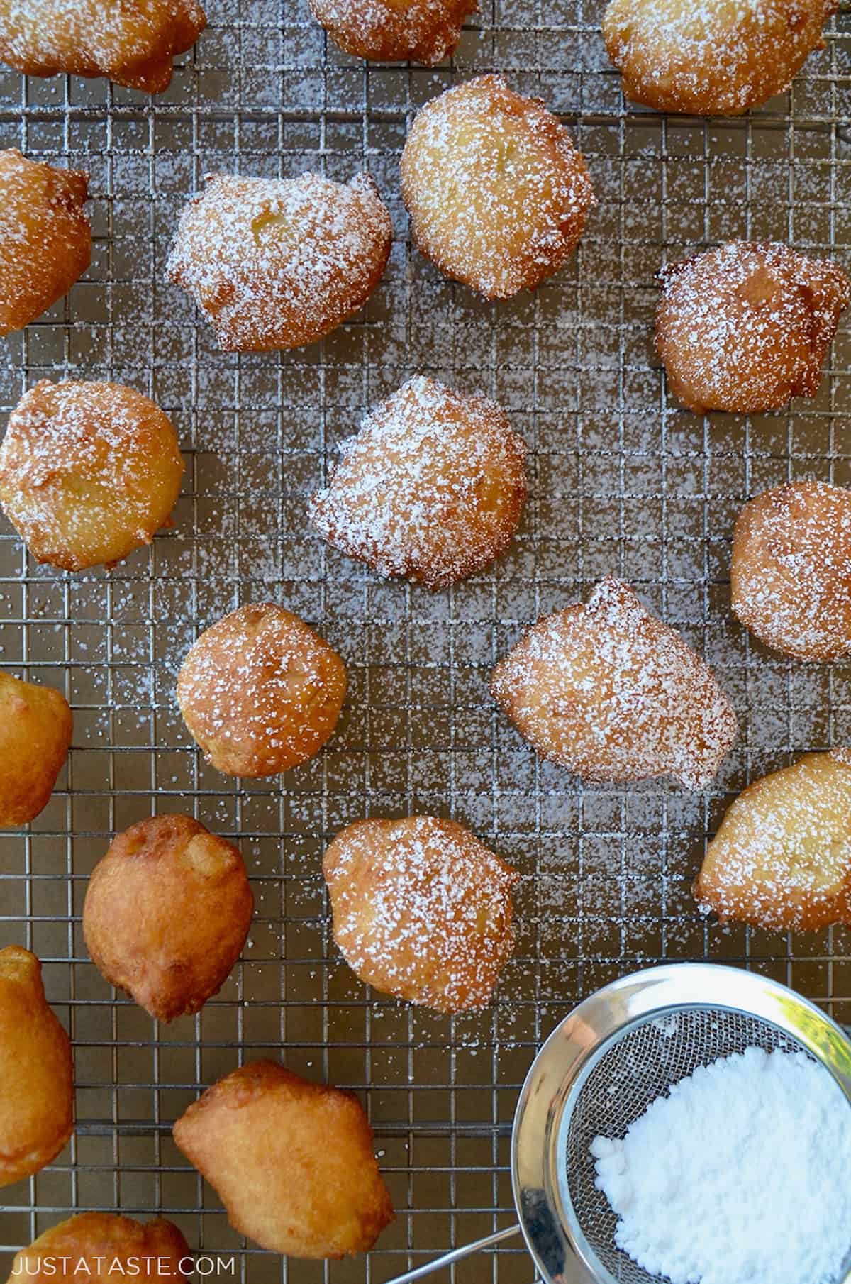 Apple fritter doughnut holes dusted with powdered sugar on a wire rack.