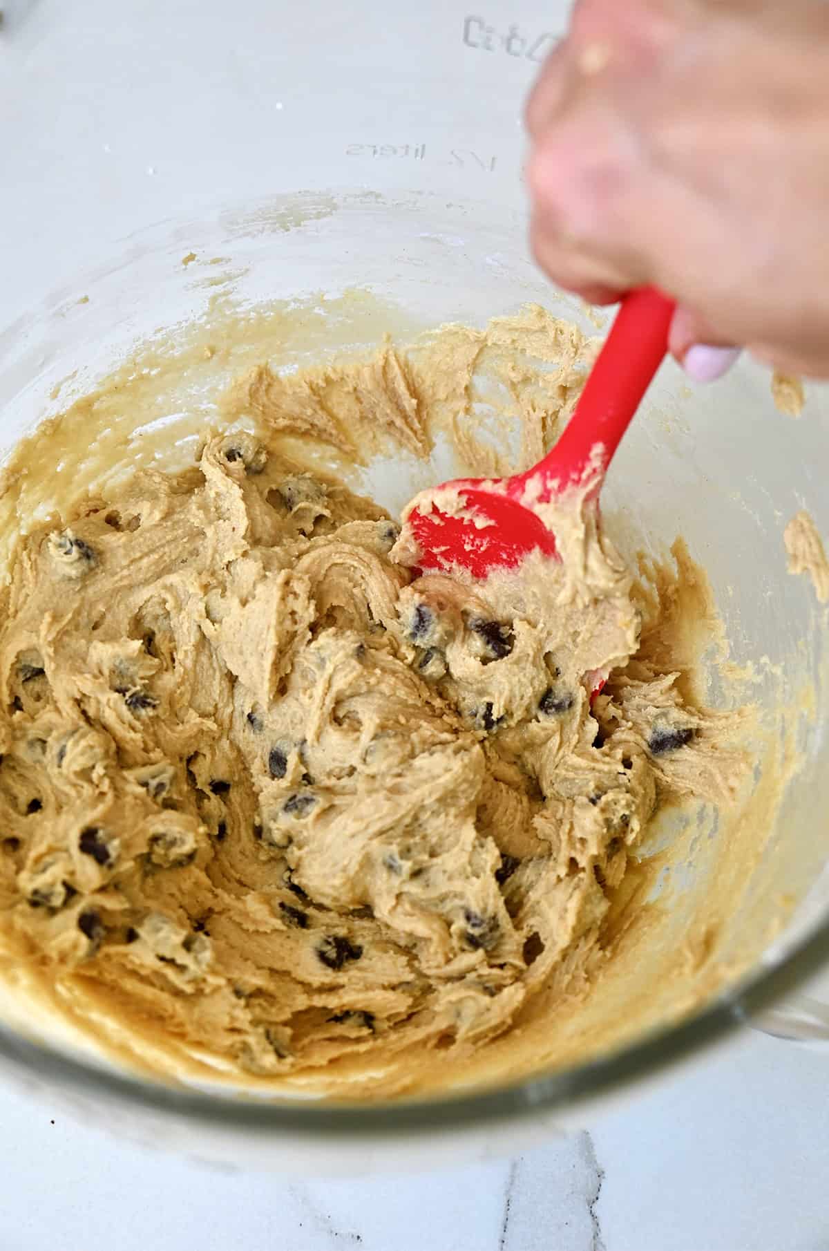 Chocolate chip cookie dough in a stand mixer bowl with a red spatula.